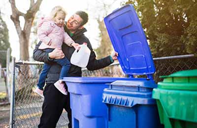 Photo of a father and daughter putting milk bottle into recycling bin