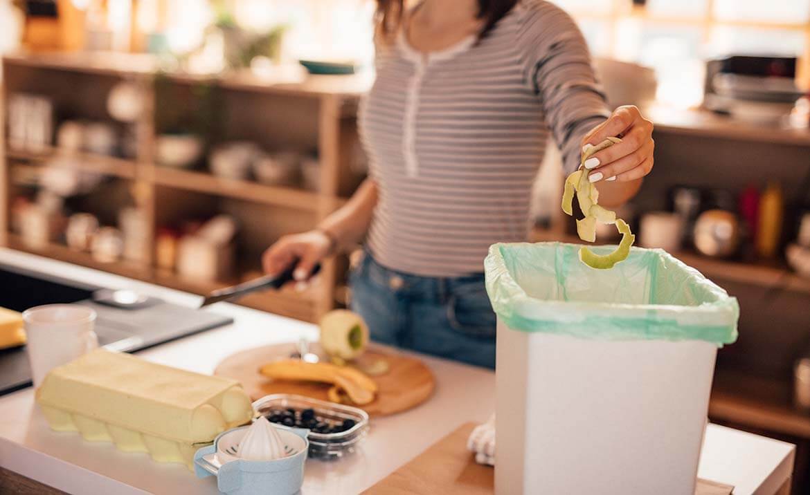 person putting food peelings into a food waste caddy